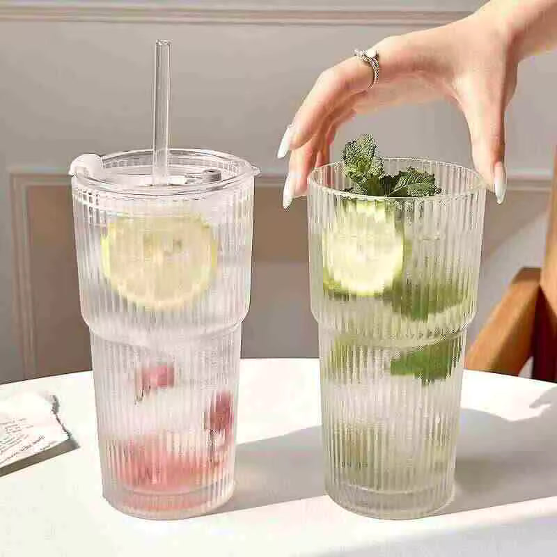 Elegant 600ml ribbed glass coffee cup with a transparent lid and glass straw, filled with iced water and fresh mint leaves on a sunlit table.