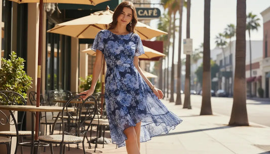 Woman in a blue floral dress standing on a sidewalk with palm trees and a cafe in the background.
