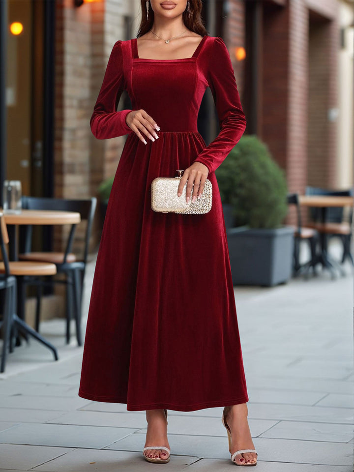 Woman wearing a red velvet dress holding a clutch in an outdoor setting.