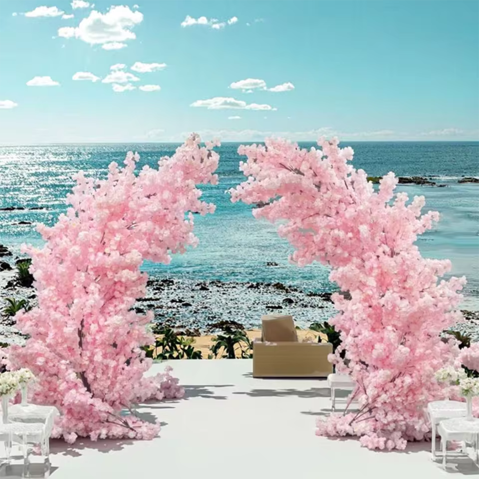 Large artificial pink cherry blossom arch for outdoor wedding ceremony decoration with a beautiful ocean and blue sky background.

