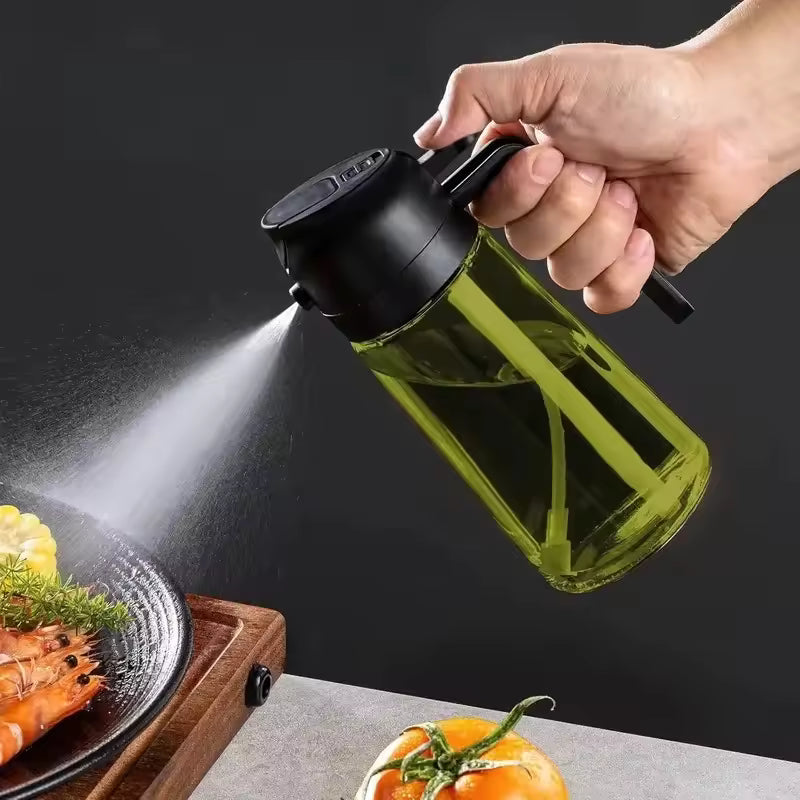 Dark green glass oil spray bottle and dispenser with a black ergonomic handle, spraying a fine mist over a plate of grilled shrimp.