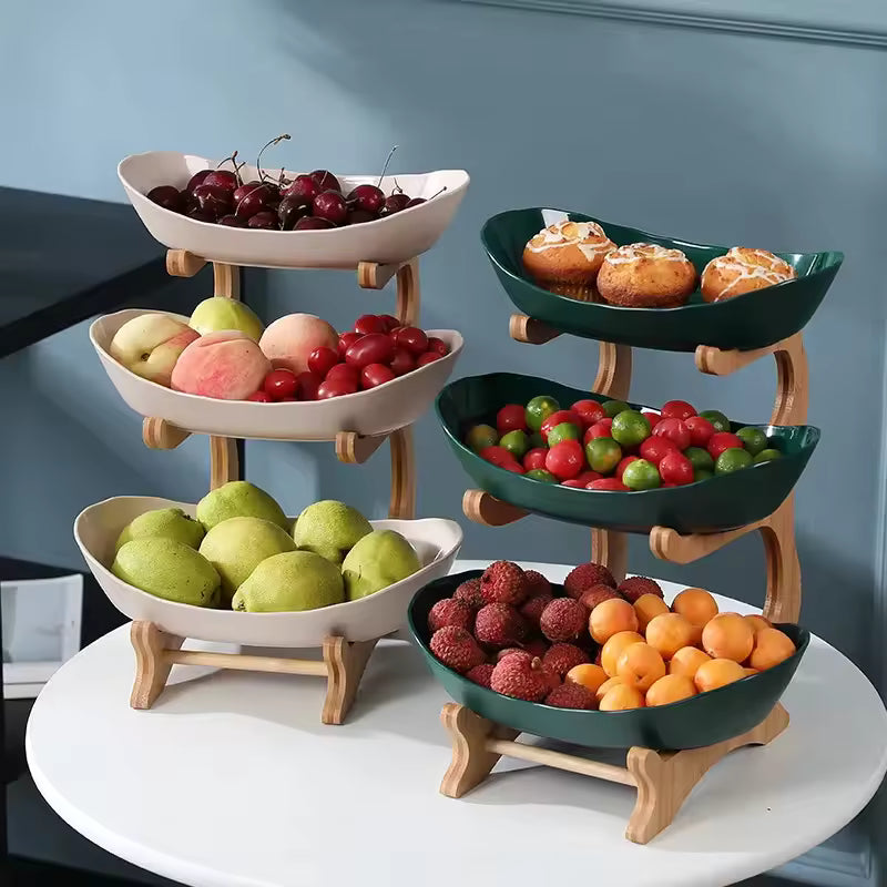 3-tier vertical serving stand with a light wood rack holding three dark green oval plates filled with fresh fruits and pastries.
