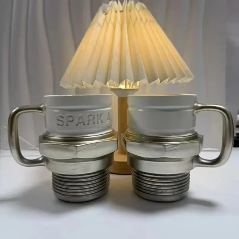 Unique silver and white coffee mug shaped like a car spark plug with an industrial handle and embossed "SPARK" text.