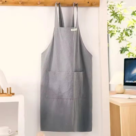Grey minimalist cotton-linen apron with cross-back straps and a large front pocket hanging on a wooden wall hook.