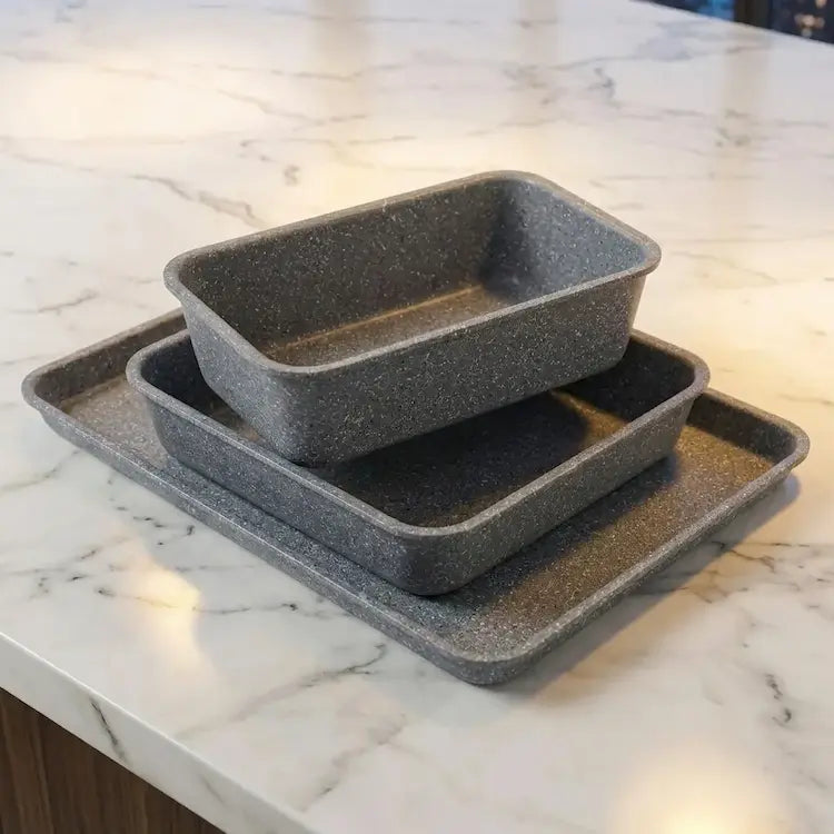 3-piece granite-coated nonstick bakeware set including loaf pan, square roasting pan, and baking sheet stacked neatly on a kitchen counter, showing thick quality edges.