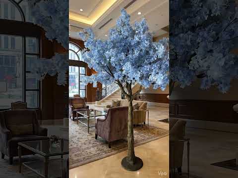 A majestic 5ft blue artificial cherry blossom tree with high-density petals, shown as a centerpiece in a luxury lobby and a formal event hall with white drapes.