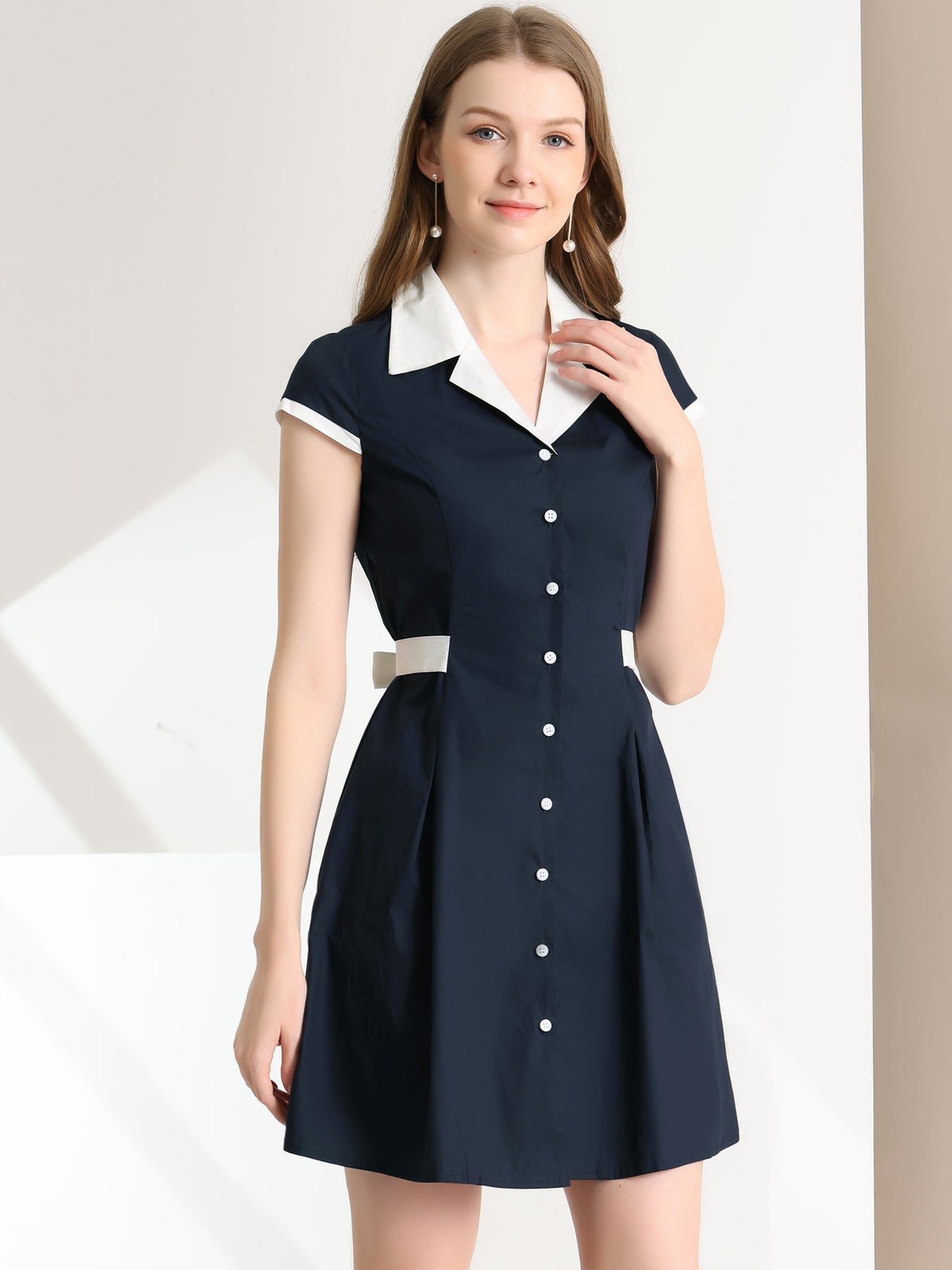 Woman wearing a navy dress with white collar and buttons on a white background