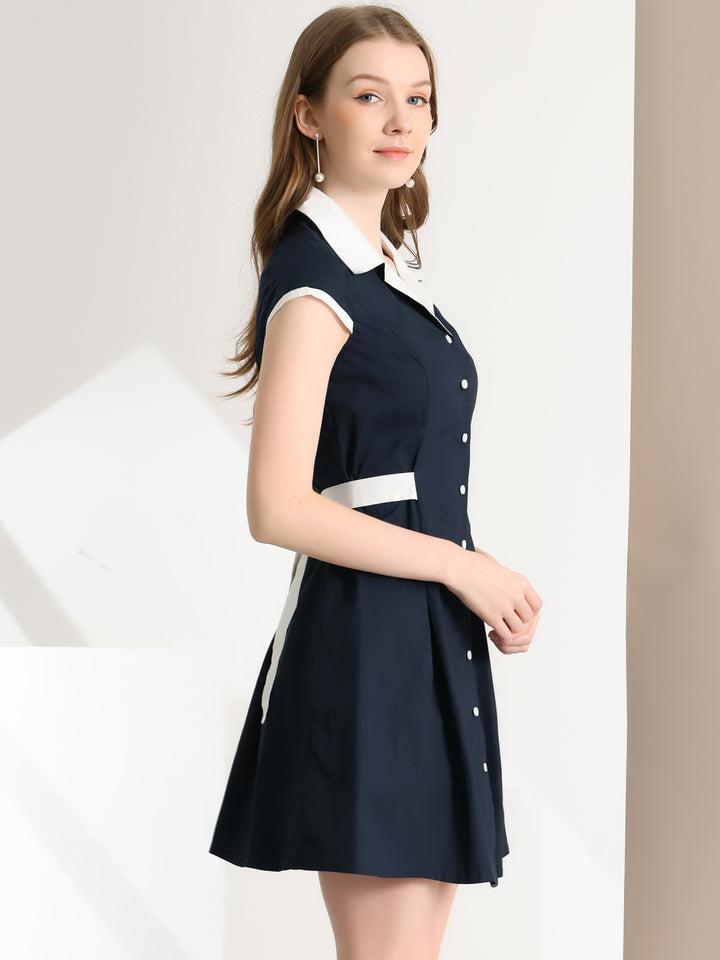 Woman wearing a navy dress with white collar and buttons on a plain background