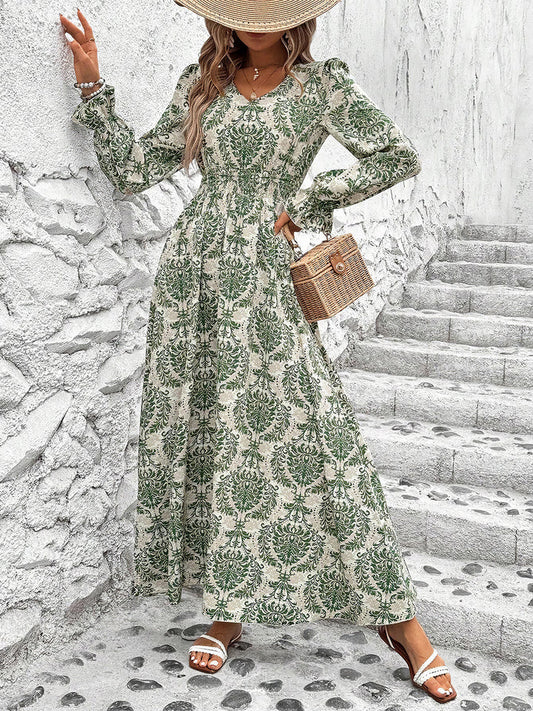 Woman in a green floral dress standing on stone steps against a white wall.