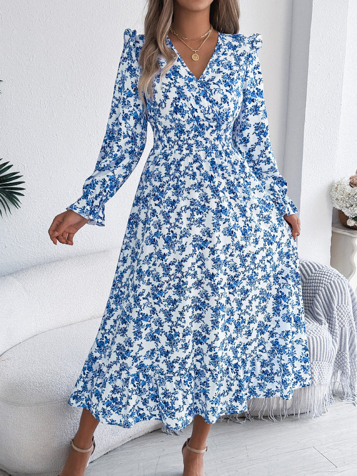 Woman wearing a blue floral dress in a room with white walls and a gray chair.