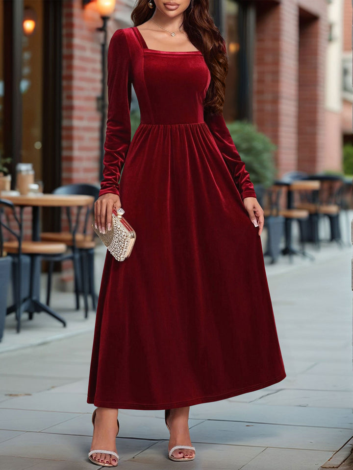 Woman wearing a burgundy dress standing outdoors near a brick building.