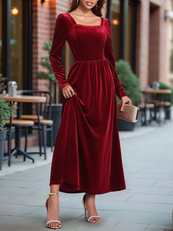 Woman wearing a red dress standing outdoors with tables and chairs in the background.