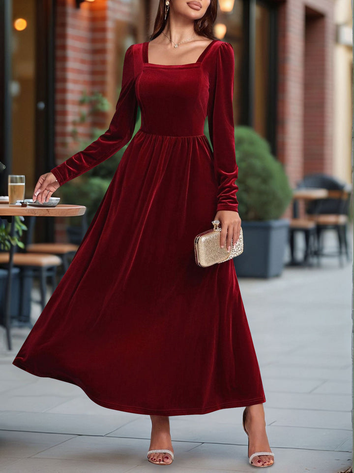 Woman wearing a burgundy velvet dress standing outdoors.